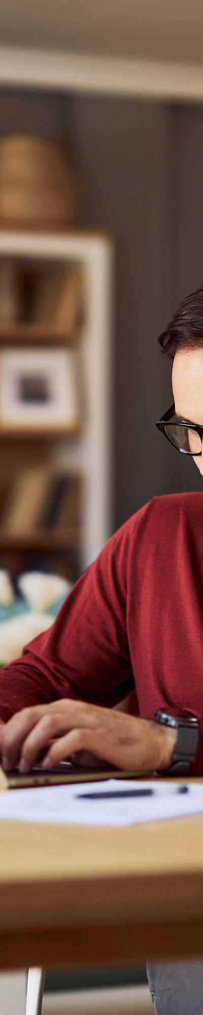 Mann mit Brille arbeitet in seinem Wohnzimmer am Laptop.