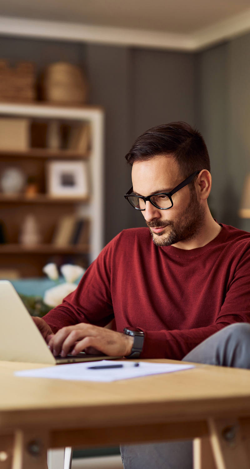 Mann mit Brille arbeitet in seinem Wohnzimmer am Laptop.