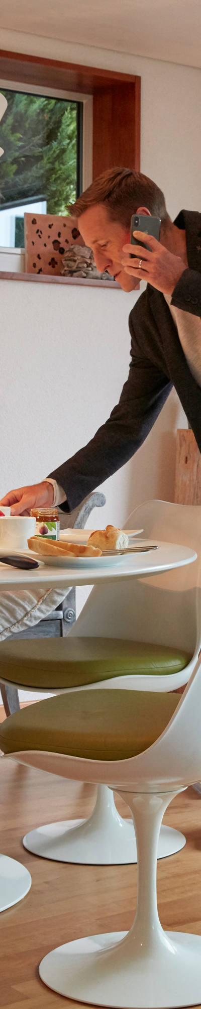Man stands with smartphone on ear at breakfast table.