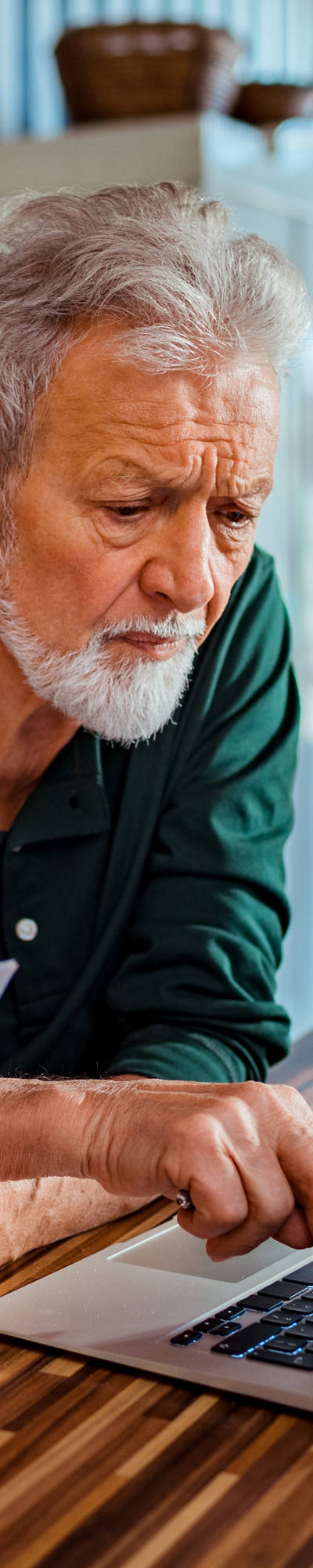 Senior man sitting at kitchen table and working on laptop