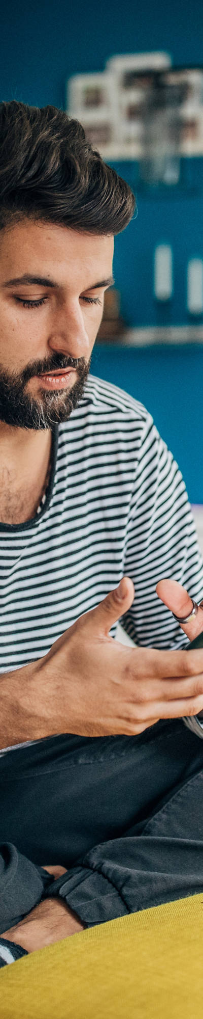 Young man sits comfortably on the armchair in the living room typing on the smartphone.
