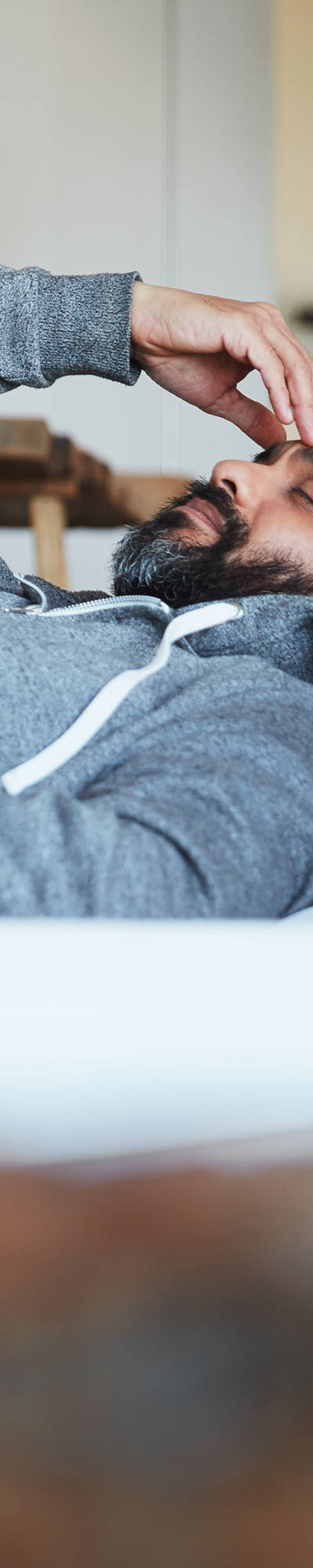 Un uomo in pigiama giace sul letto con gli occhi chiusi e si tiene una mano sulla fronte.