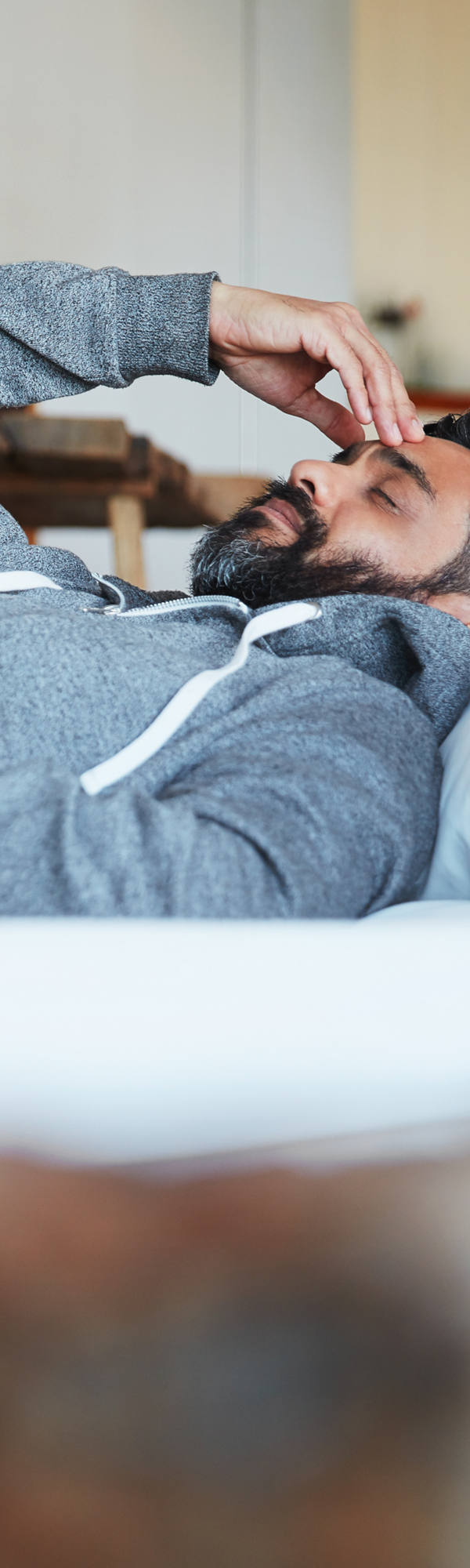 A man in pajamas lies on the bed with his eyes closed and holds his forehead with one hand.