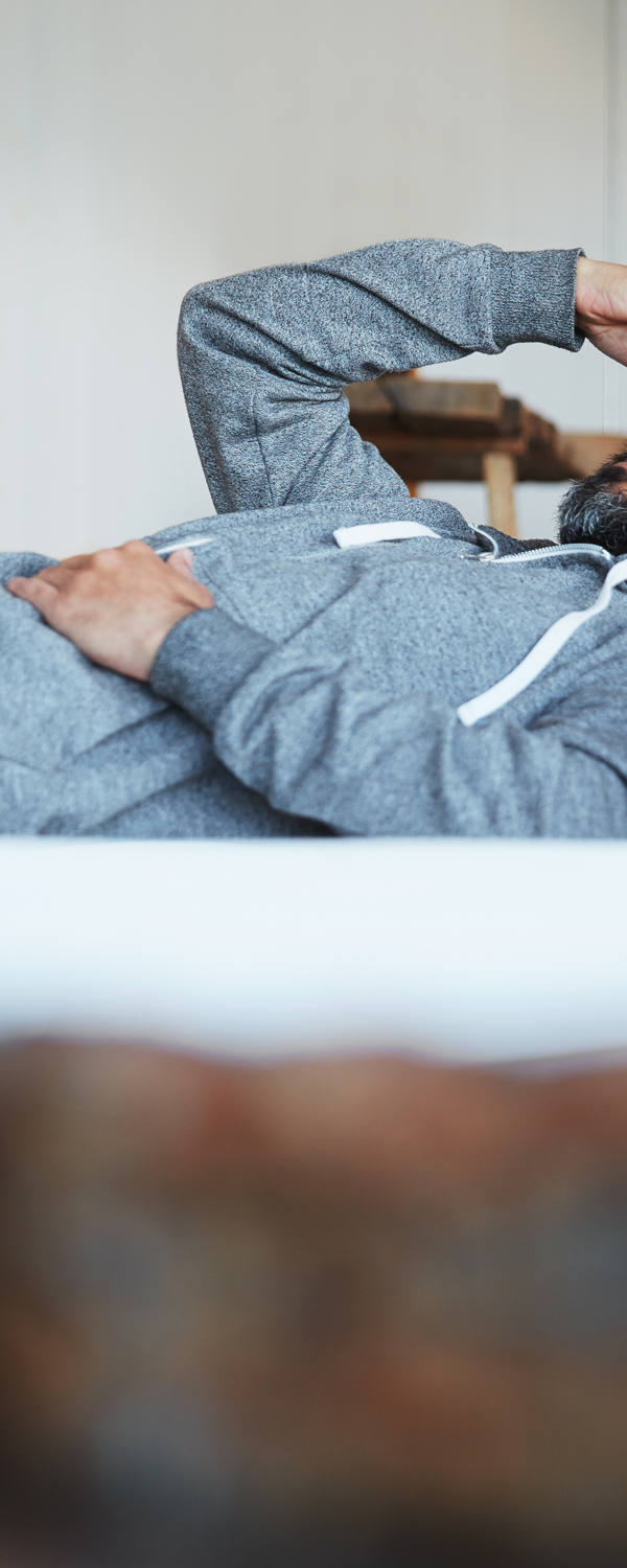 Un homme en pyjama est couché sur le lit, les yeux fermés et se tient le front d’une main.