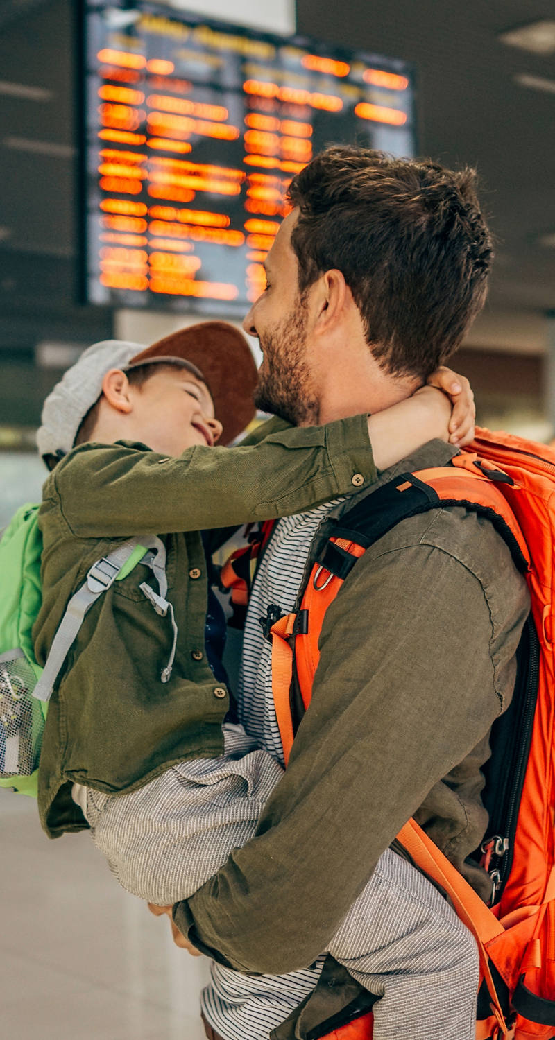 Father carries his son at the airport. Both carry a backpack.
