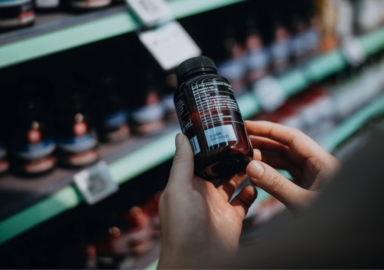Une femme se tient devant une étagère dans la droguerie et tient une boîte de médicaments en lisant les ingrédients.