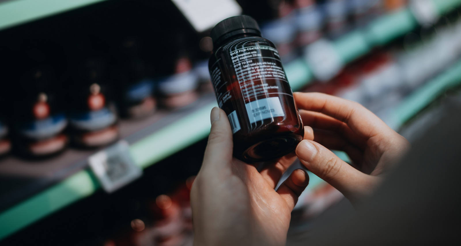 Eine Frau steht in der Drogerie vor einem Regal und hält eine Dose Medikamente in Händen während Sie die Inhaltsstoffe liest.