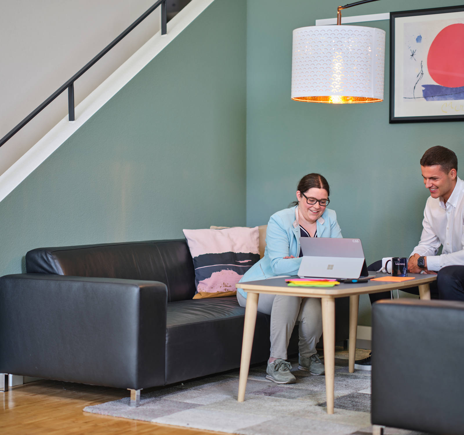Eine Frau und ein Mann sitzen auf Sofas und schauen in einen Laptop.