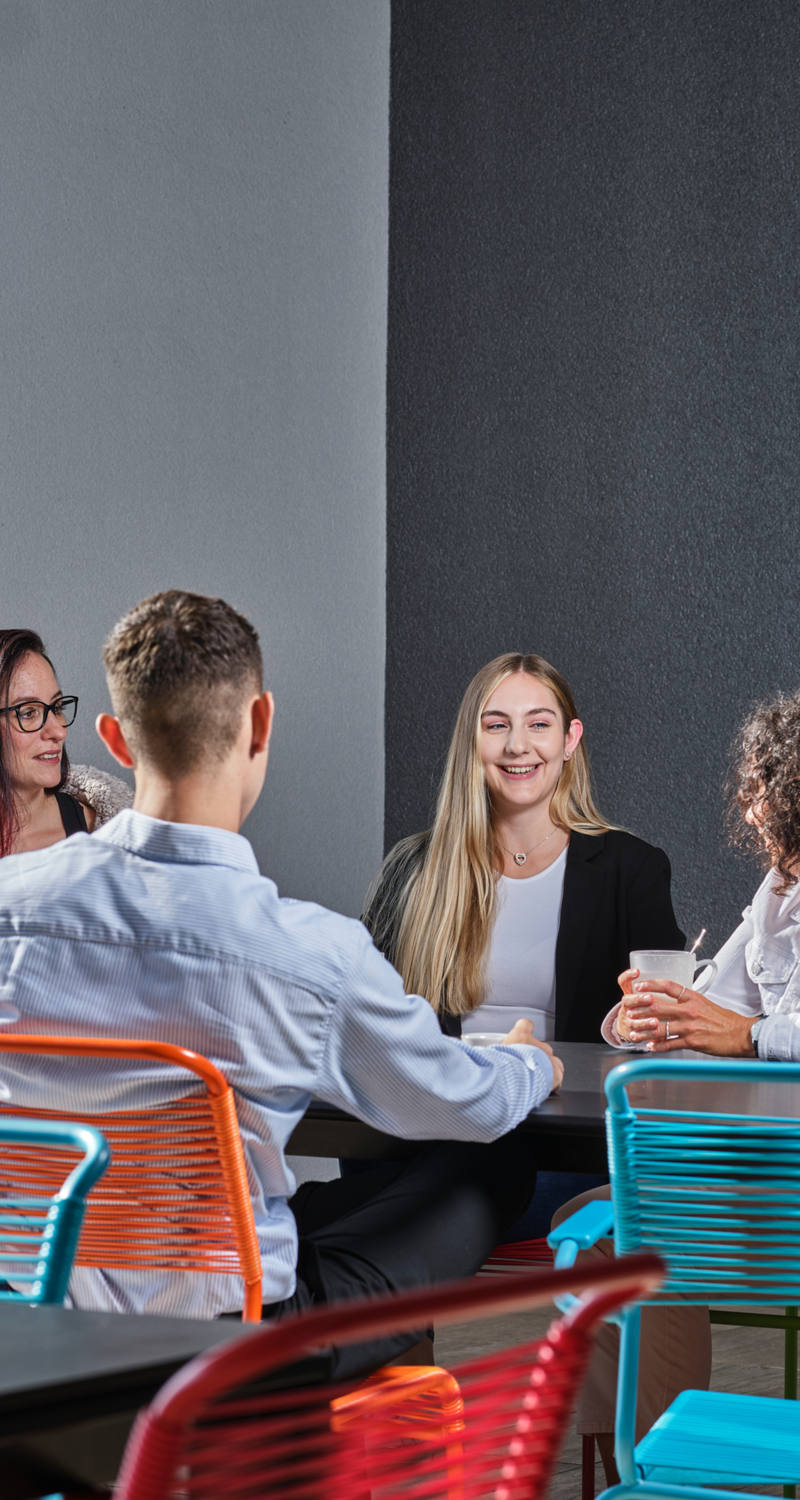 Eine Gruppe von Arbeitskollegen sitzen auf den bunten Outdoor-Stühlen der CSS Terrasse und geniessen eine Pause.