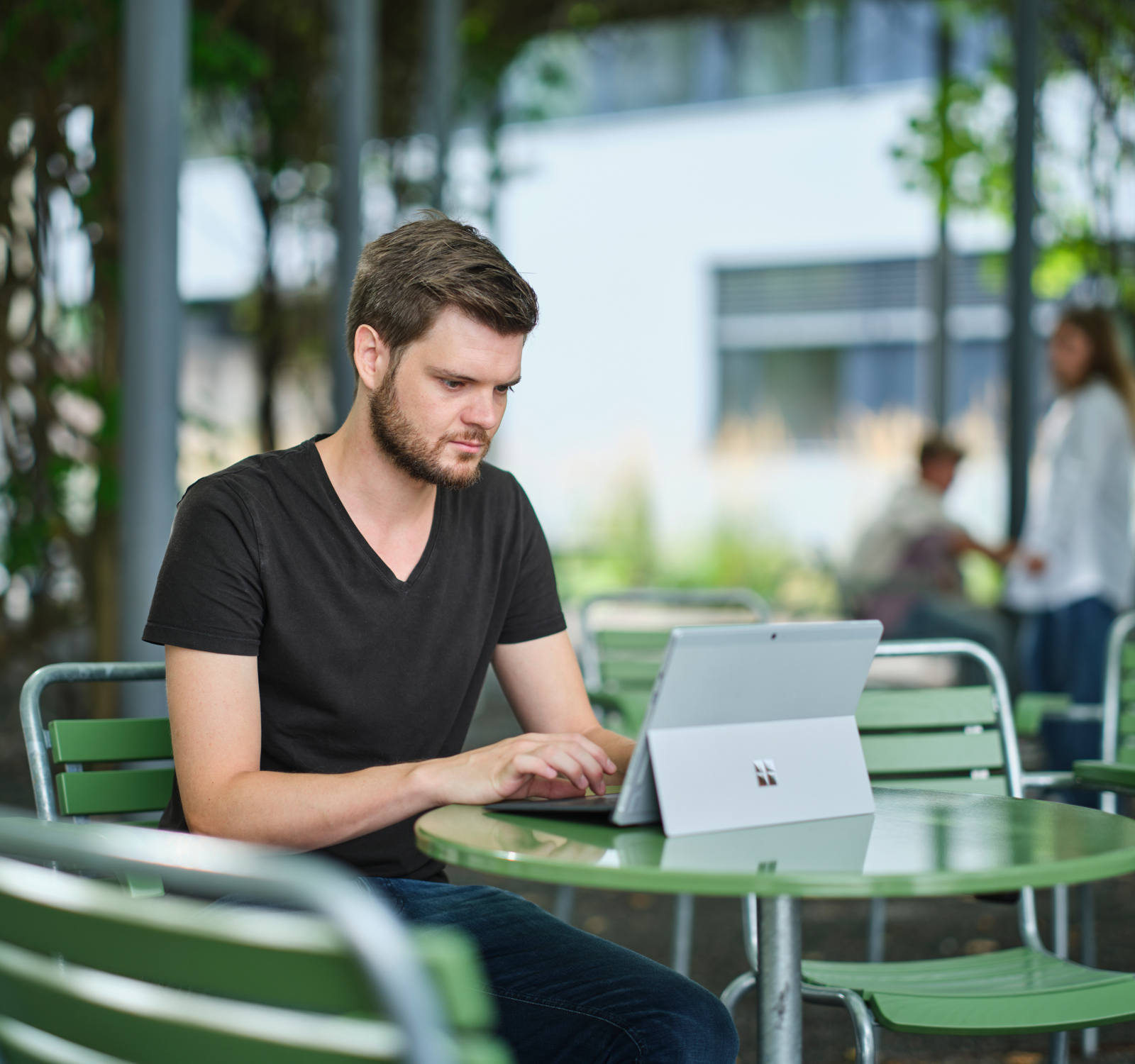 Un homme est assis sur une chaise verte et travaille sur son ordinateur portable dans un parc verdoyant.