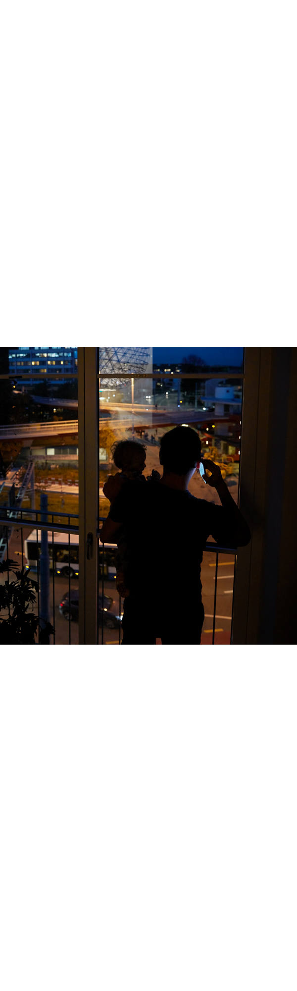 Father on the phone with child on his arm at night.