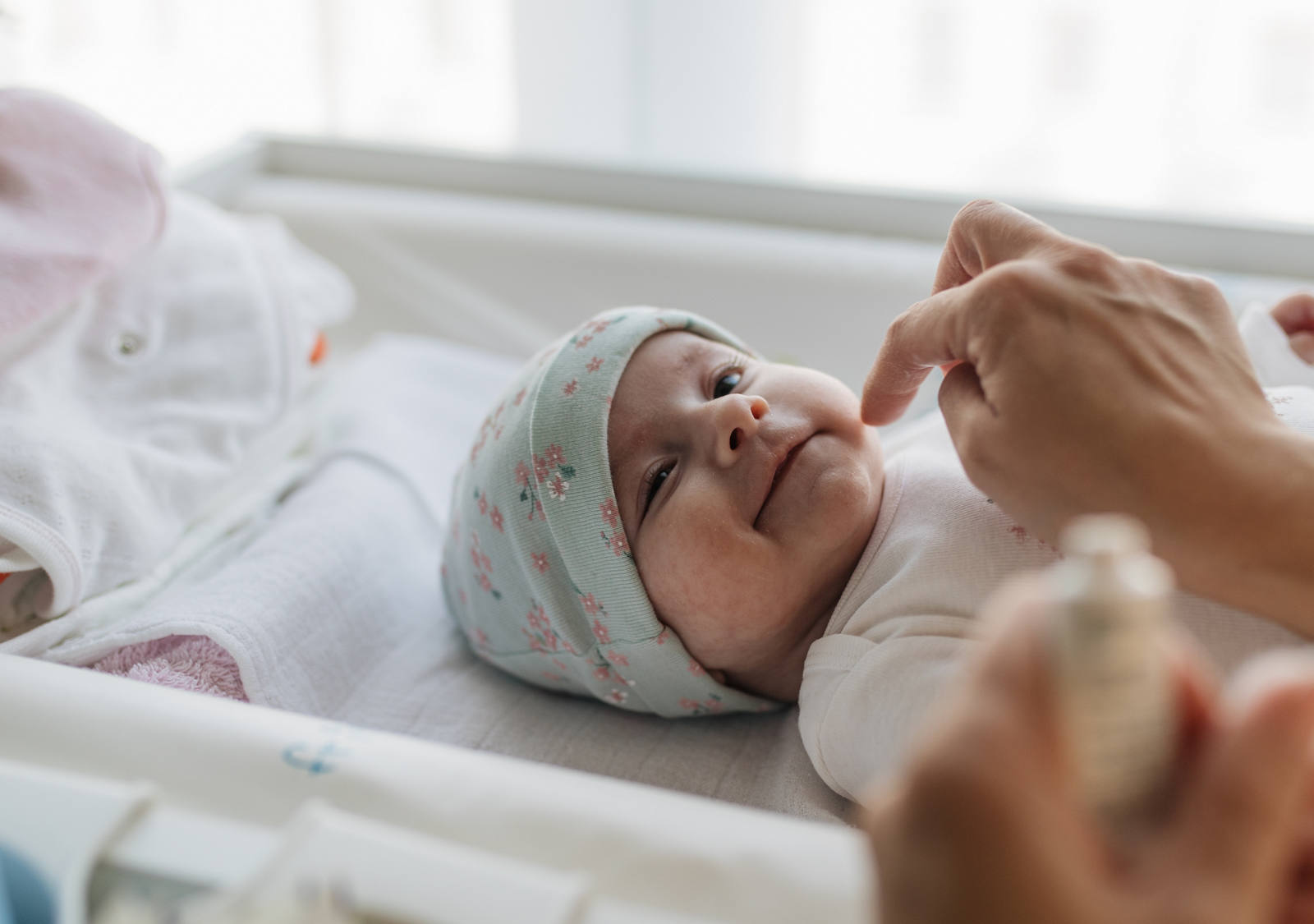 Neugeborenes Baby liegt im Bettchen und wird von einem Erwachsenen mit Salbe eingecremt.