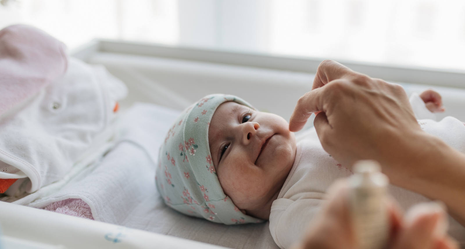 Newborn baby is lying in the crib and is creamed with ointment by an adult.