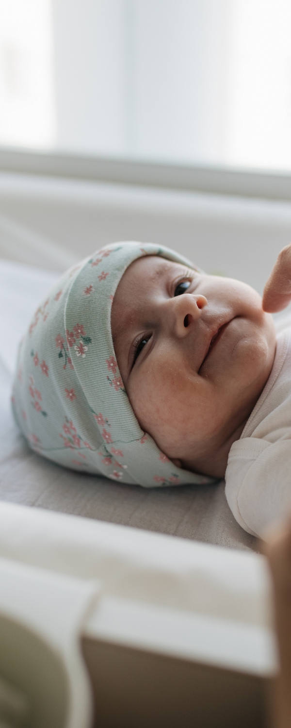 Neugeborenes Baby liegt im Bettchen und wird von einem Erwachsenen mit Salbe eingecremt.
