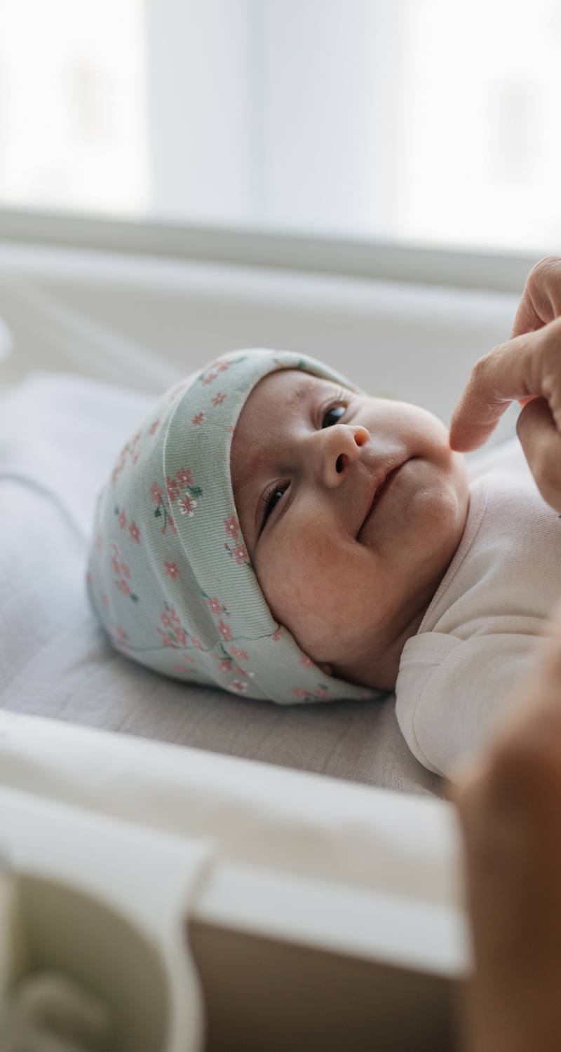 Neugeborenes Baby liegt im Bettchen und wird von einem Erwachsenen mit Salbe eingecremt.