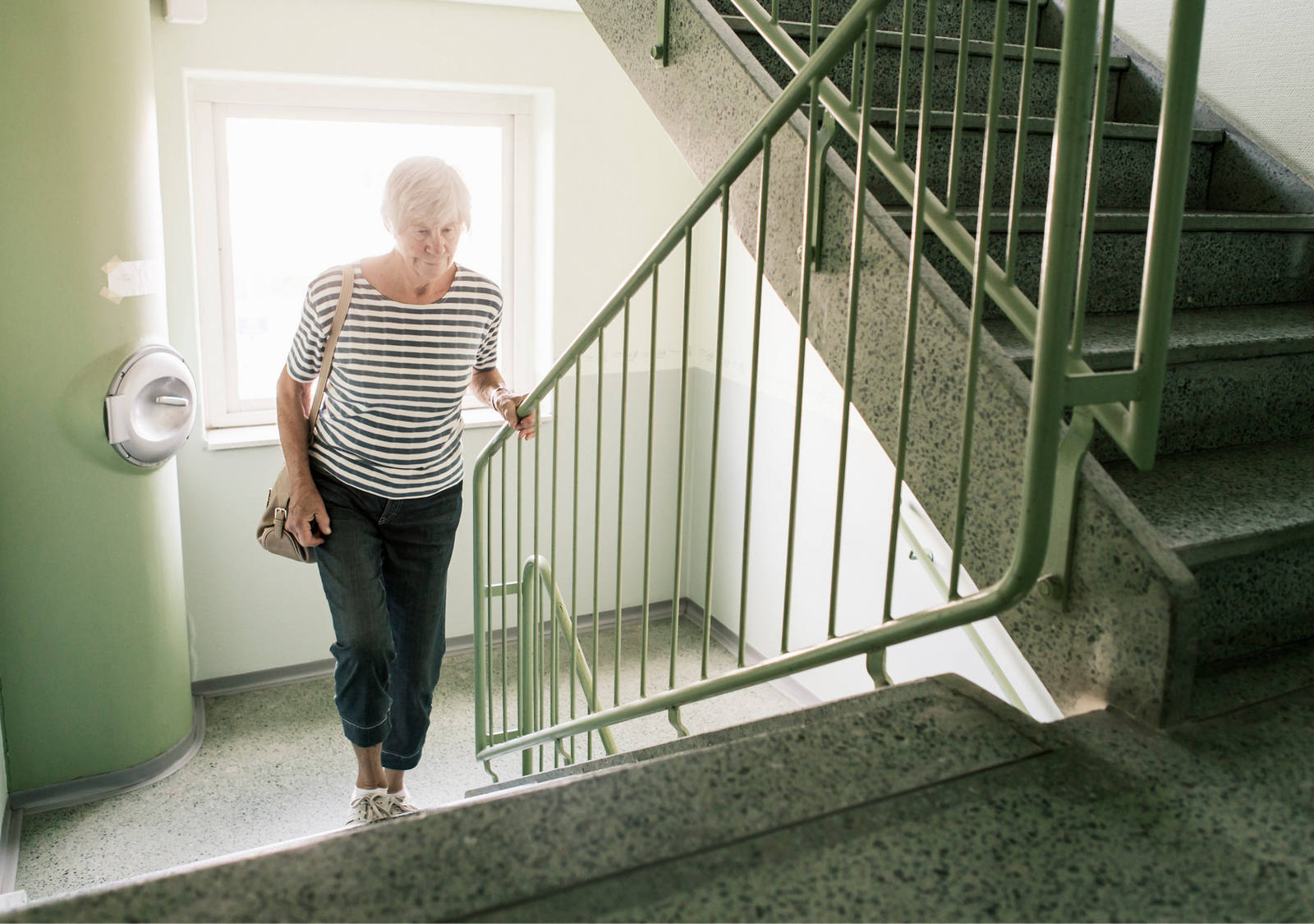 Older woman running in the stairwell and holding on to the handrail.