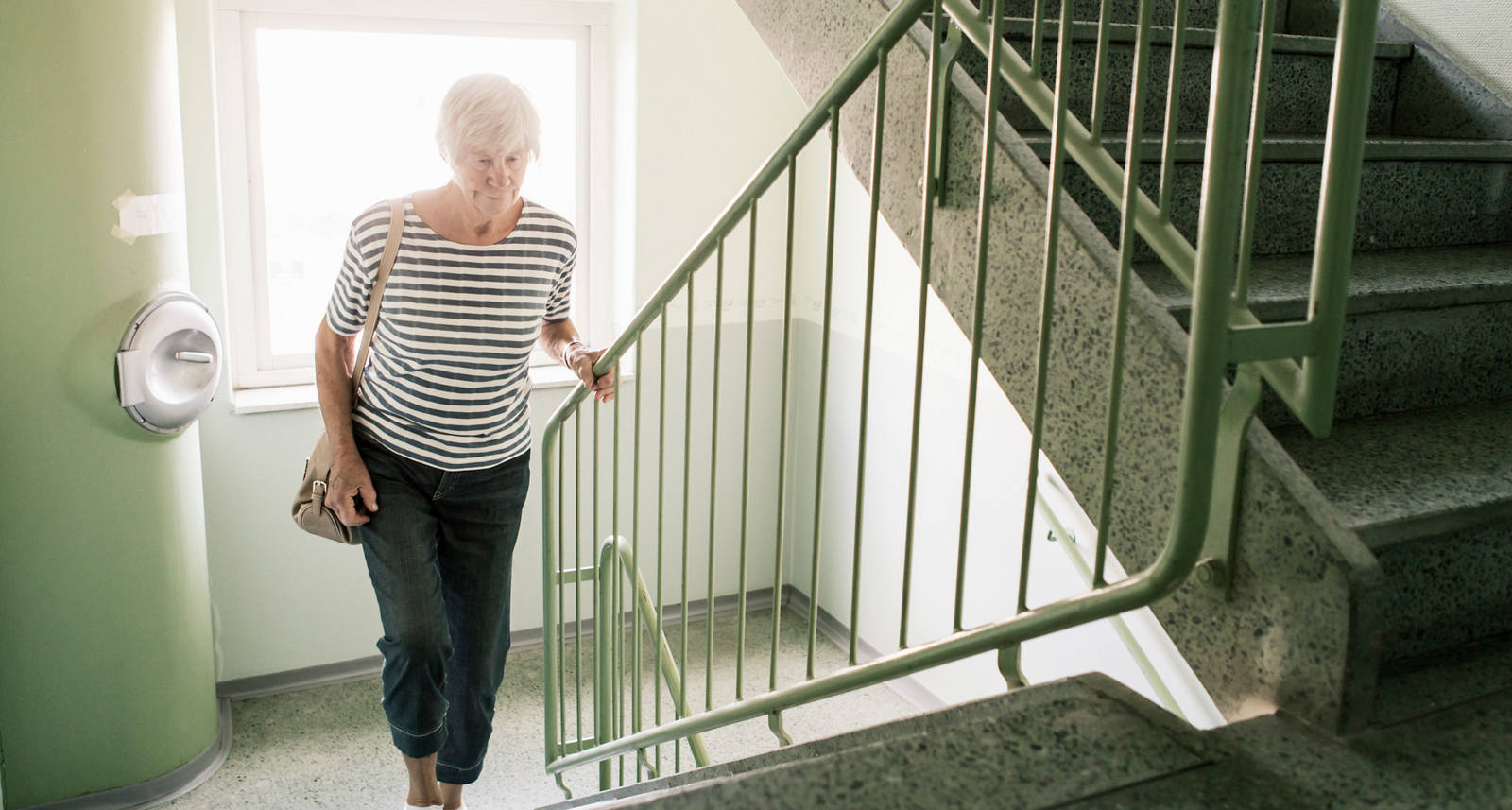 Donna anziana corre nelle scale e si aggrappa al corrimano.