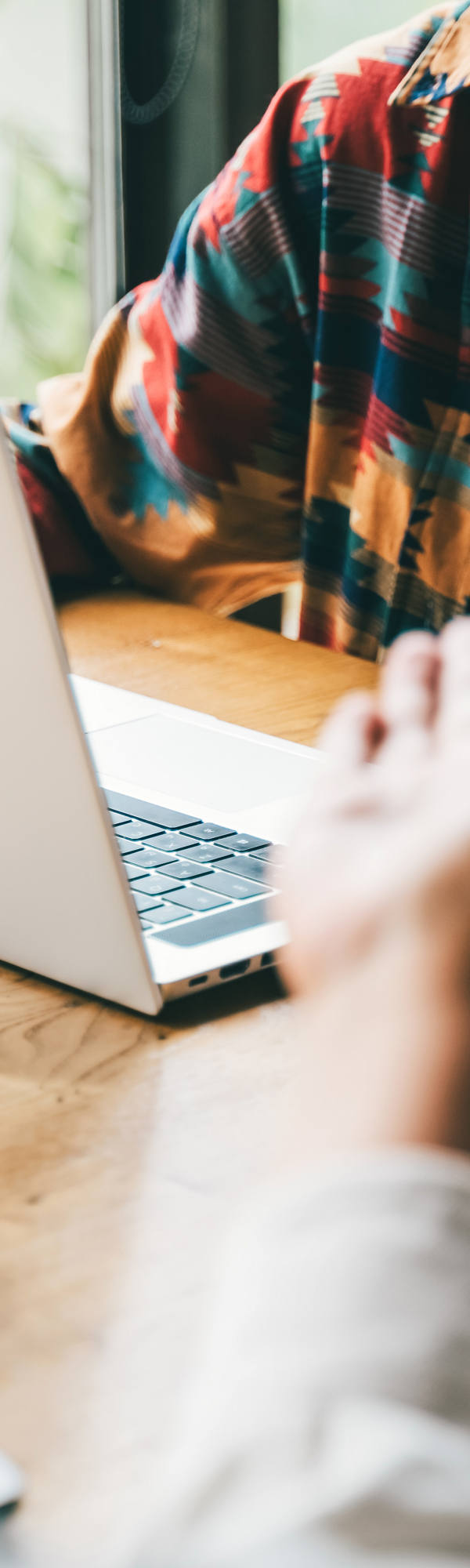 Two people with a laptop are sitting at a small table discussing and gesturing with their hands.