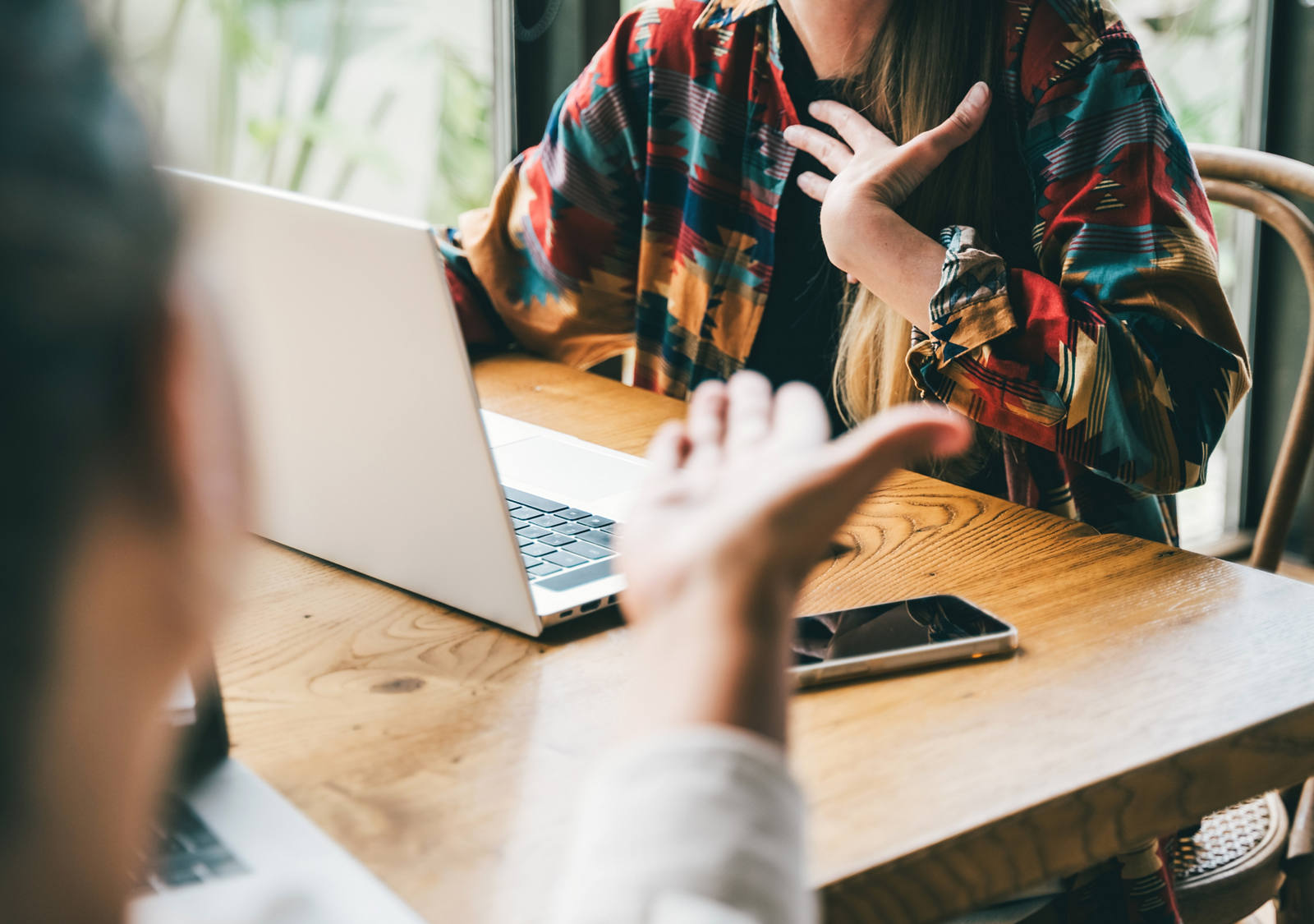 Zwei Personen mit Laptop sitzen an einem kleinen Tisch und führen eine Diskussion und gestikulieren mit den Händen.