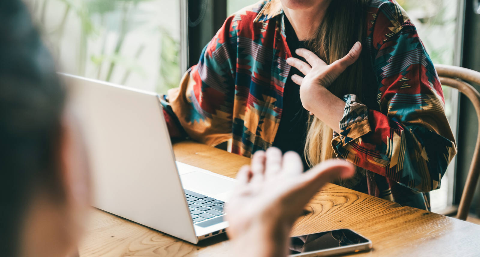 Zwei Personen mit Laptop sitzen an einem kleinen Tisch und führen eine Diskussion und gestikulieren mit den Händen.