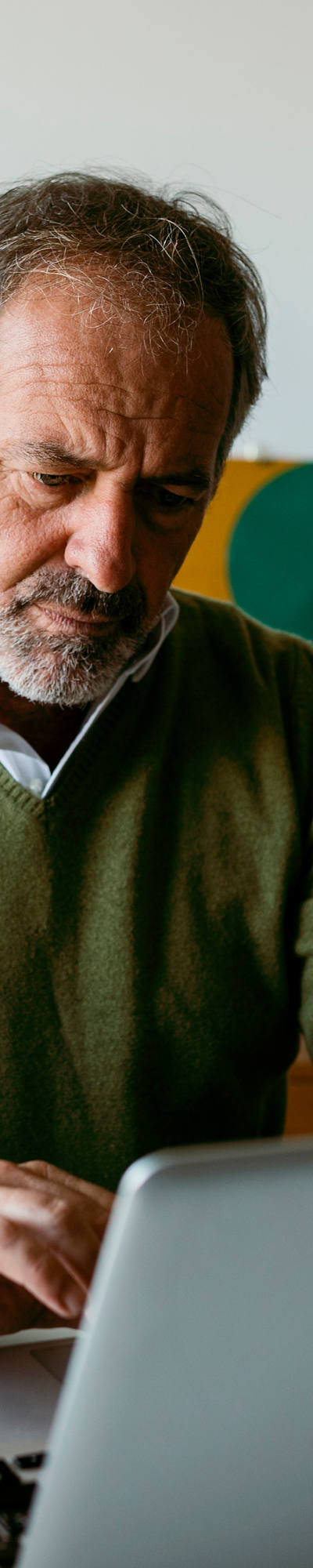 Un homme d’âge mûr est assis dans son bureau à la maison et travaille sur son ordinateur portable. Autour de lui, il y a beaucoup de plantes vertes.