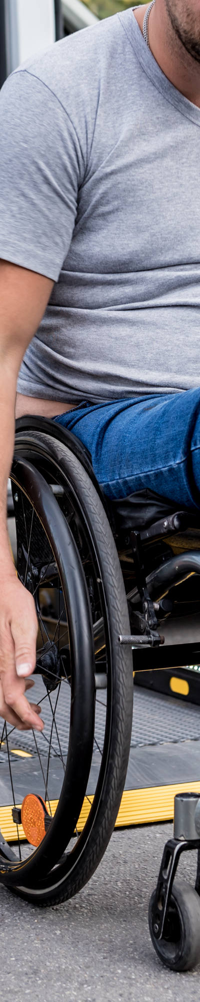 Man in wheelchair drives backwards on lifting platform of transport bus.