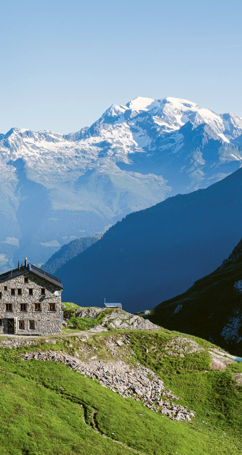 SAC Terrihütte auf einem grasbedeckten Hügel in einer Alpenlandschaft.