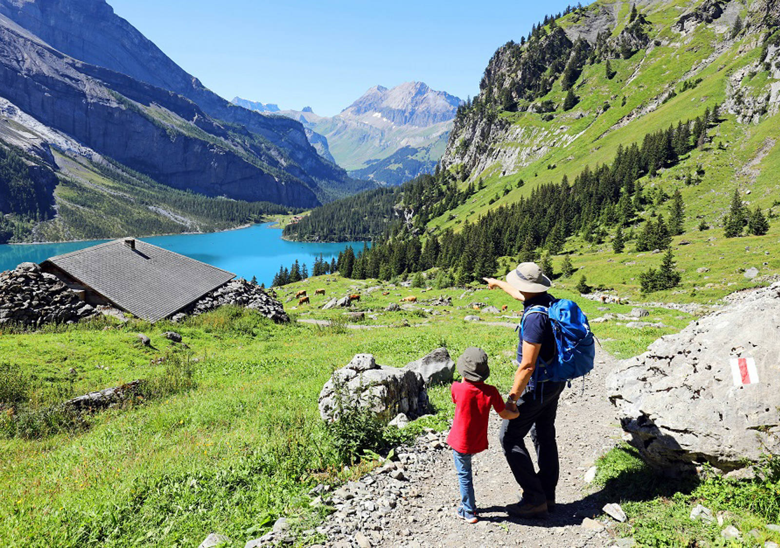 Father and child stand on a hiking trail and look down into the valley to the mountain lake.