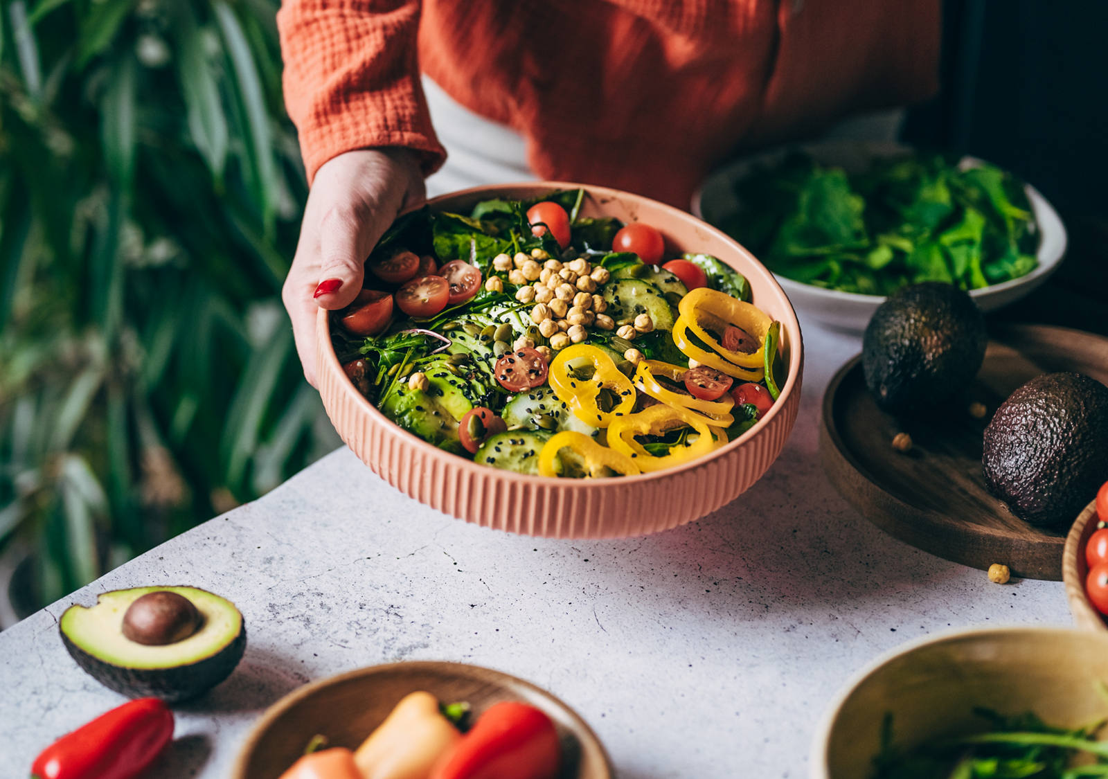 Eine Frau steht in der Küche und hält eine Salat-Bowl in die Kamera. Die Schüssel ist gefüllt mit verschiedenem und butem Gemüse und Kichererbsen.