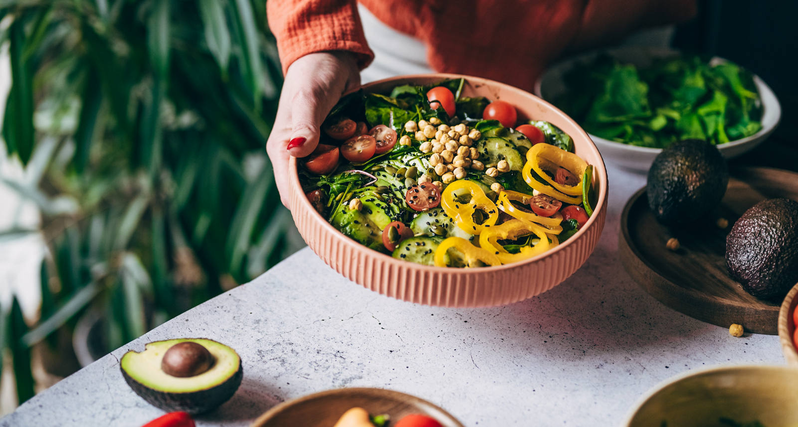 Eine Frau steht in der Küche und hält eine Salat-Bowl in die Kamera. Die Schüssel ist gefüllt mit verschiedenem und butem Gemüse und Kichererbsen.