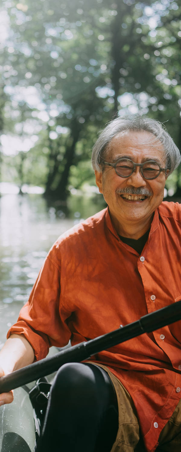 Un homme âgé est joyeusement assis dans un kayak et pagaie sur une rivière le long des arbres et des parois rocheuses sous le soleil.