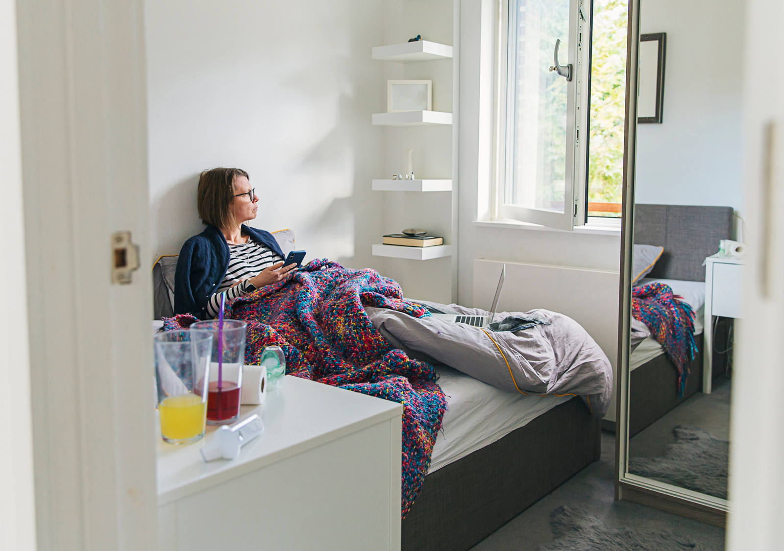 Une femme est allongée dans son lit, malade, et regarde par la fenêtre.