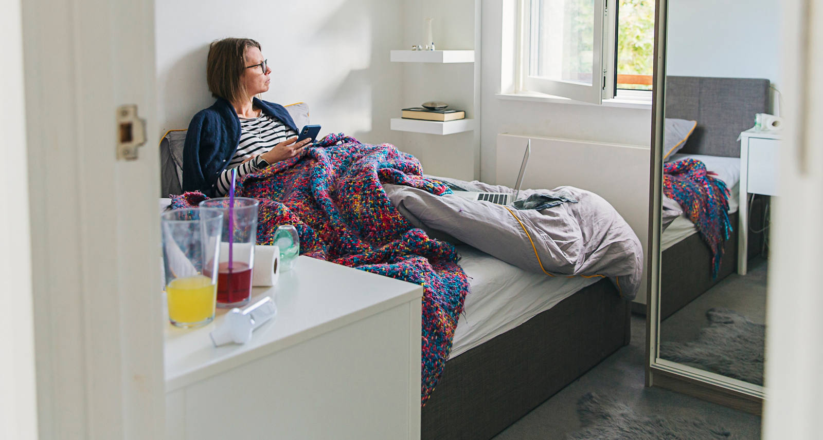 Una donna è a letto ammalata e guarda fuori dalla finestra.