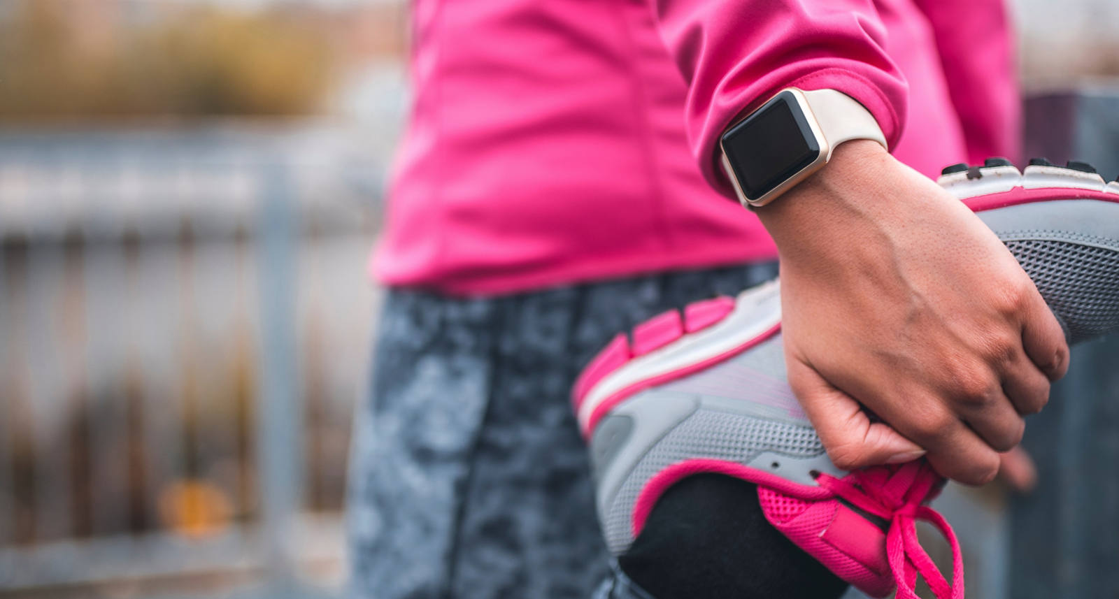 Eine Frau in pinker Sportkleidung hält ihren linken Fuss, dehnt ihr Bein und hat eine Smartwatch am Handgelenk.