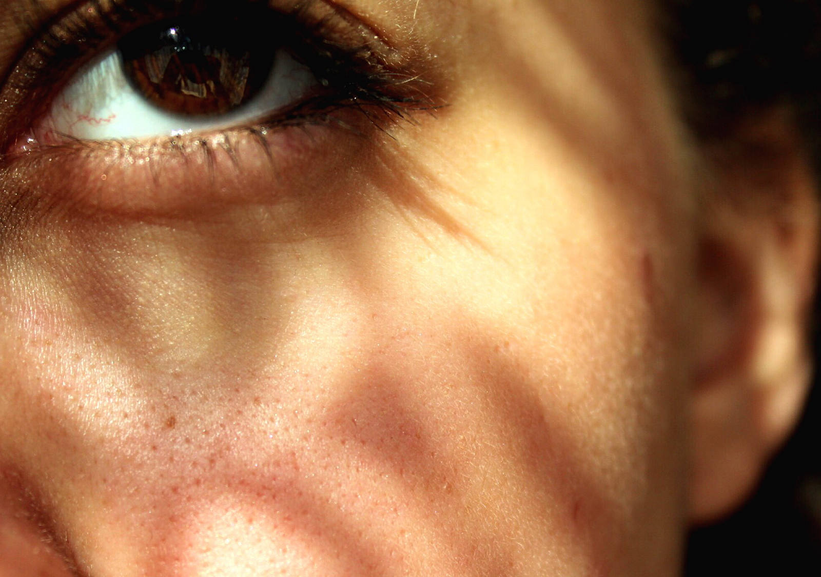 Close-up of the left side of the face of a woman shining the sun on her face.