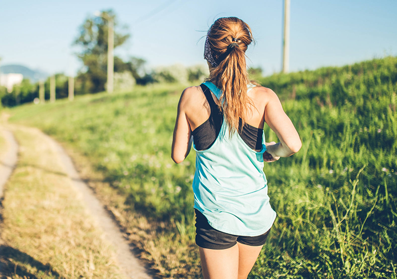 Une jeune femme en tenue de sport courte court au soleil le long d’un chemin de campagne.