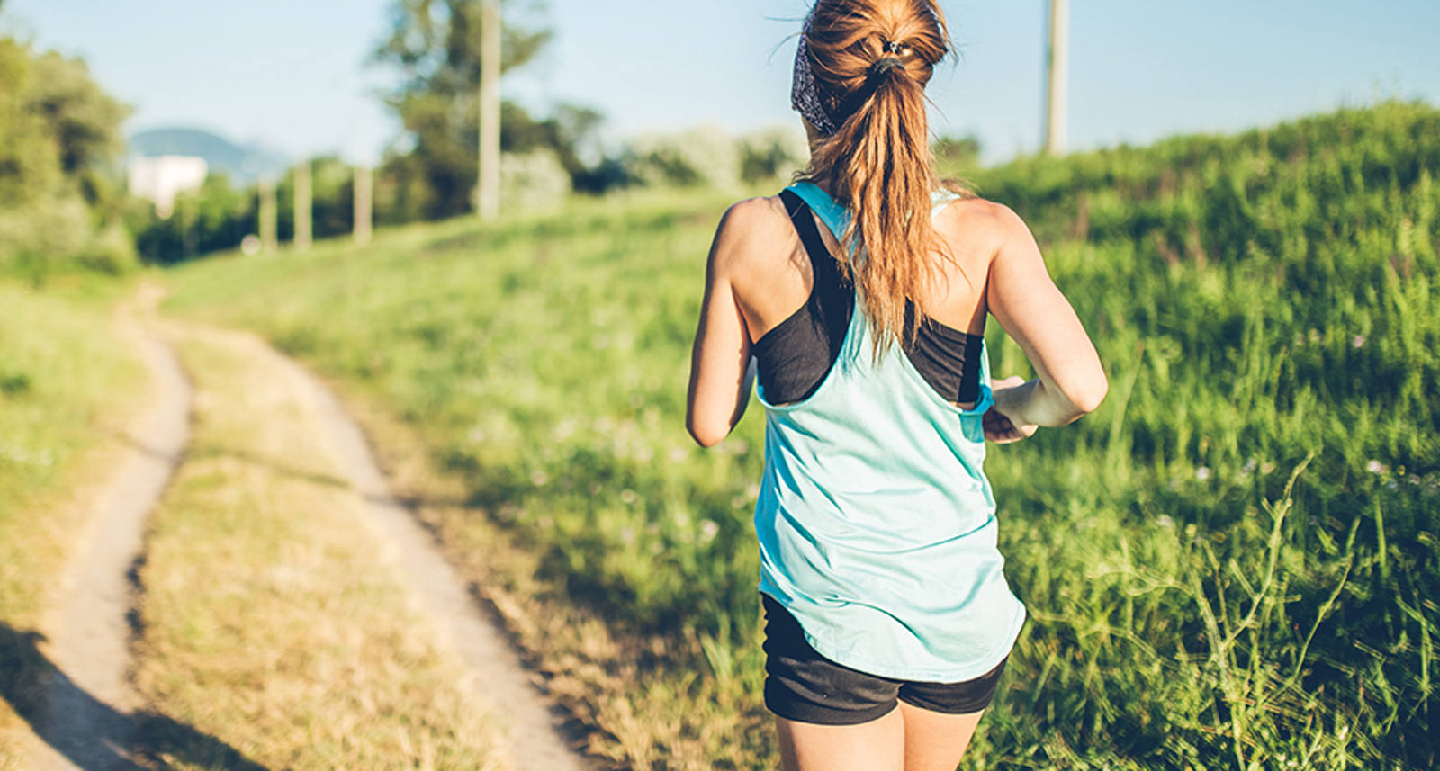 Une jeune femme en tenue de sport courte court au soleil le long d’un chemin de campagne.
