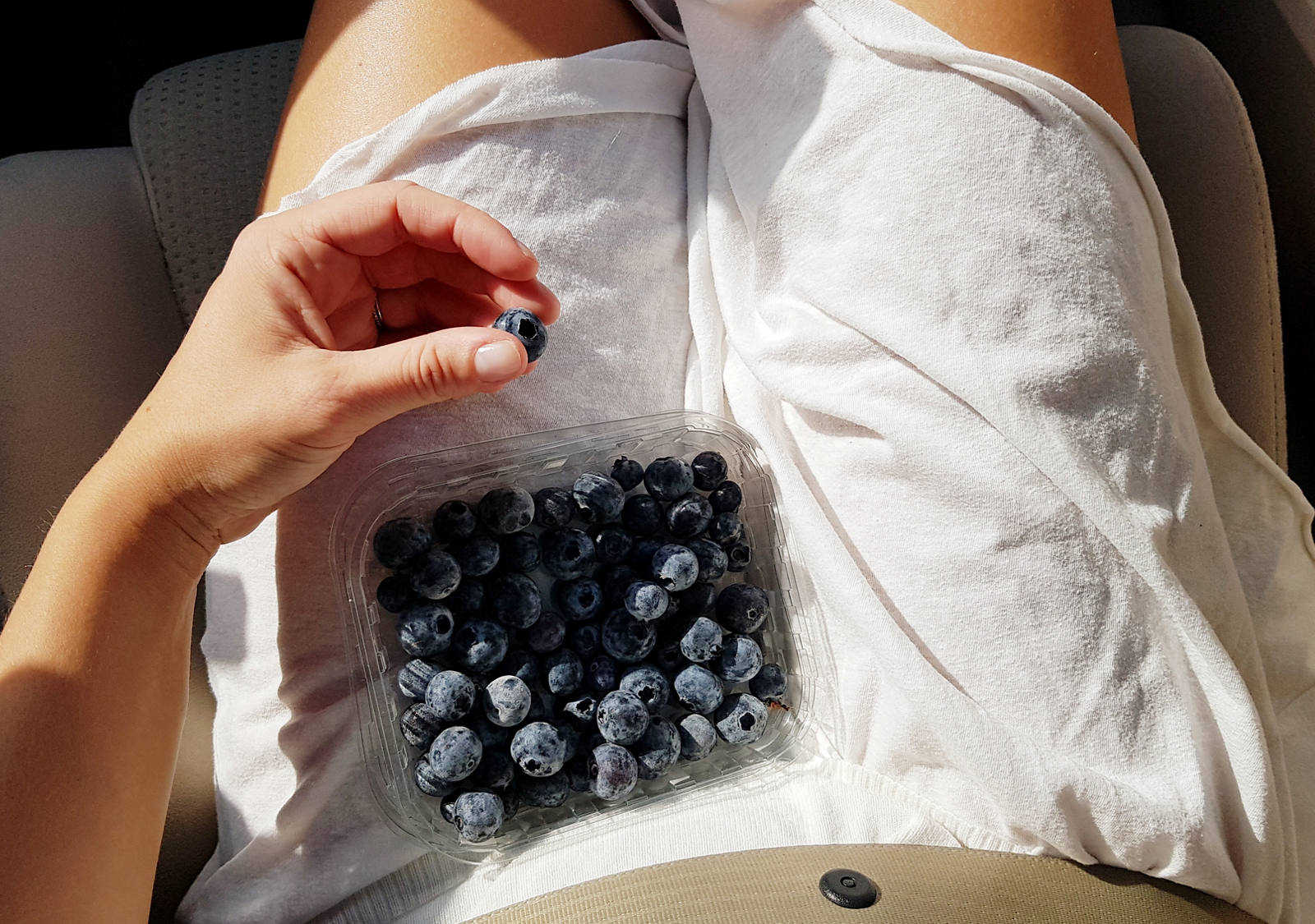 A woman in the car has a box of blueberry on her lap.
