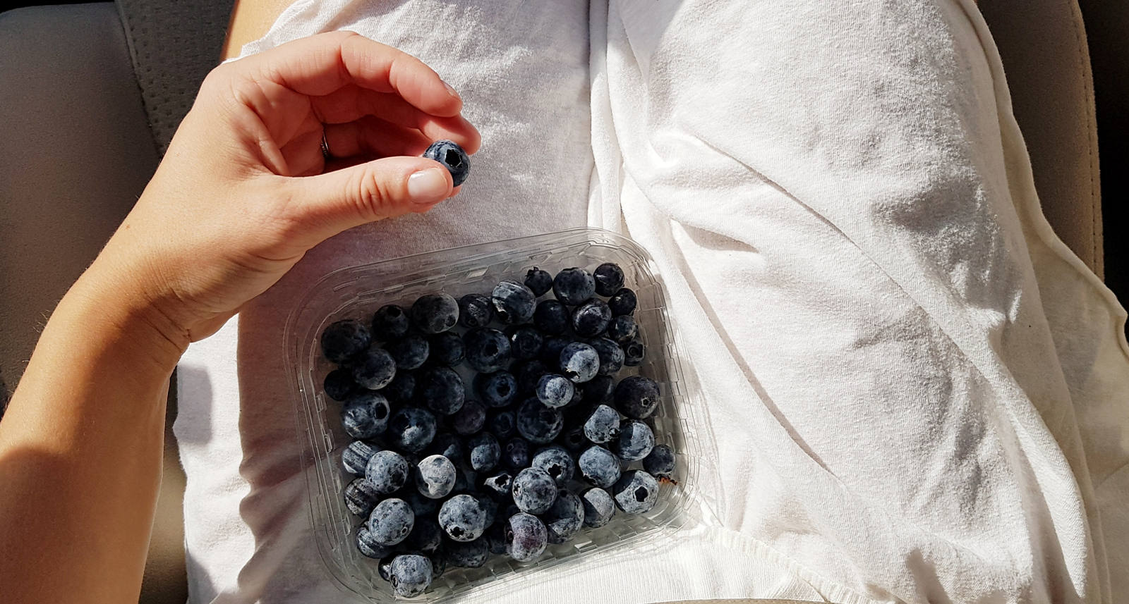 A woman in the car has a box of blueberry on her lap.