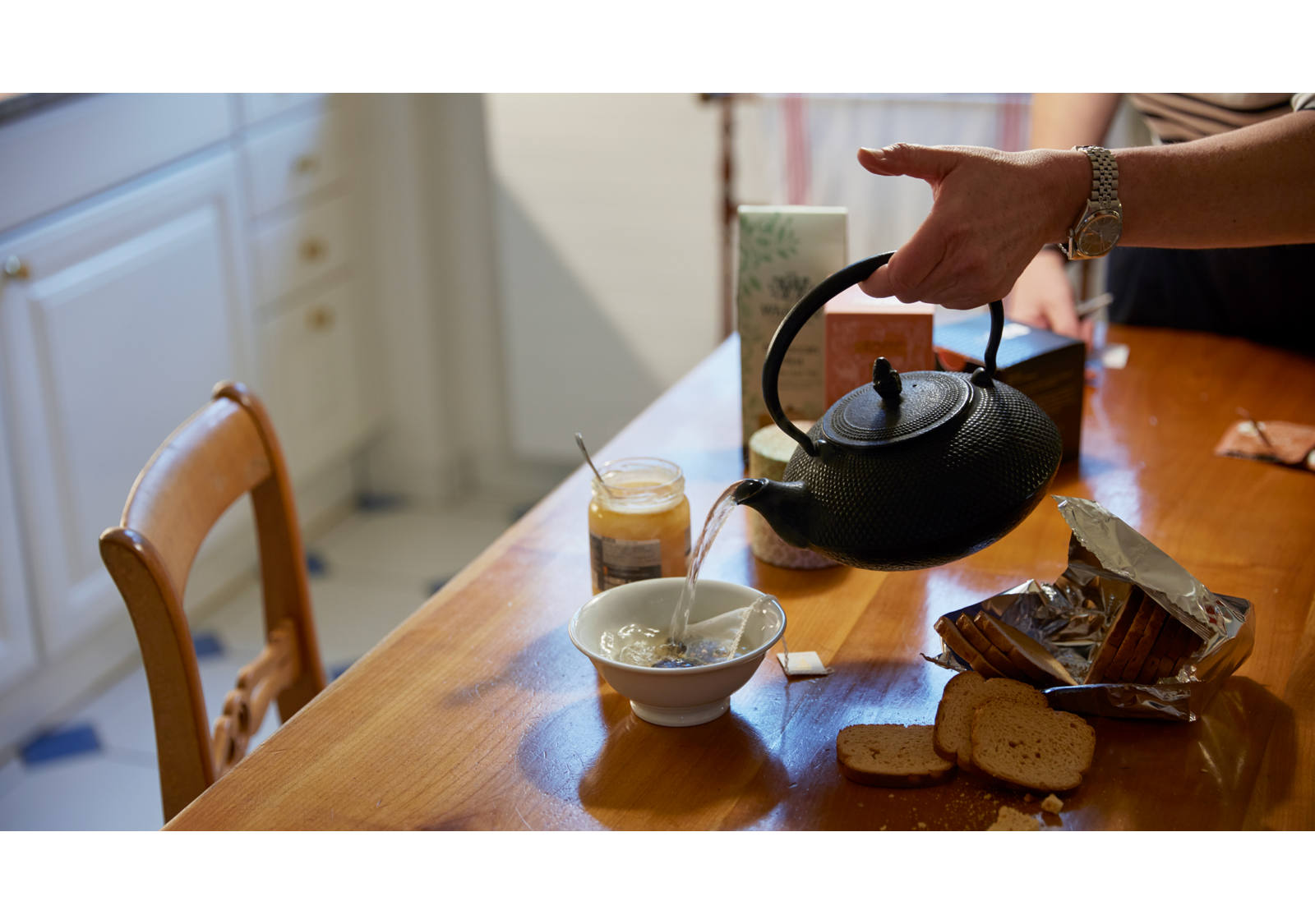 A la table de la cuisine, une femme verse de l’eau chaude dans une tasse de thé.