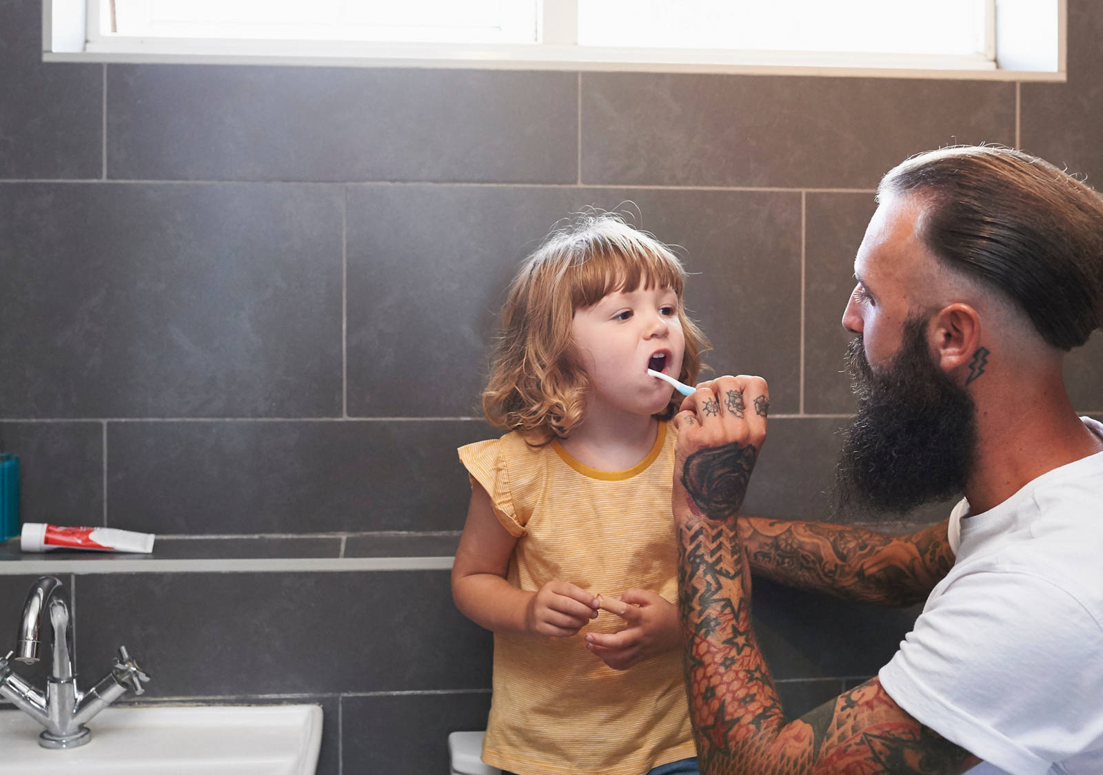  In the bathroom, the father brushes his daughter’s teeth.