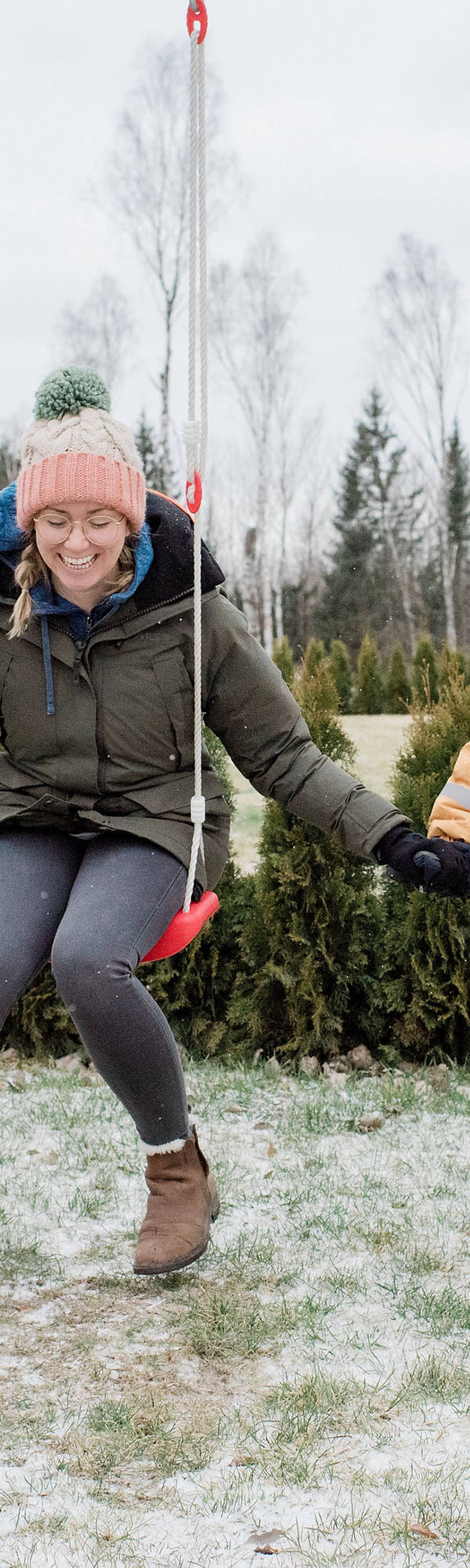 Donna con bambino calorosamente avvolto in abiti invernali su un’altalena.