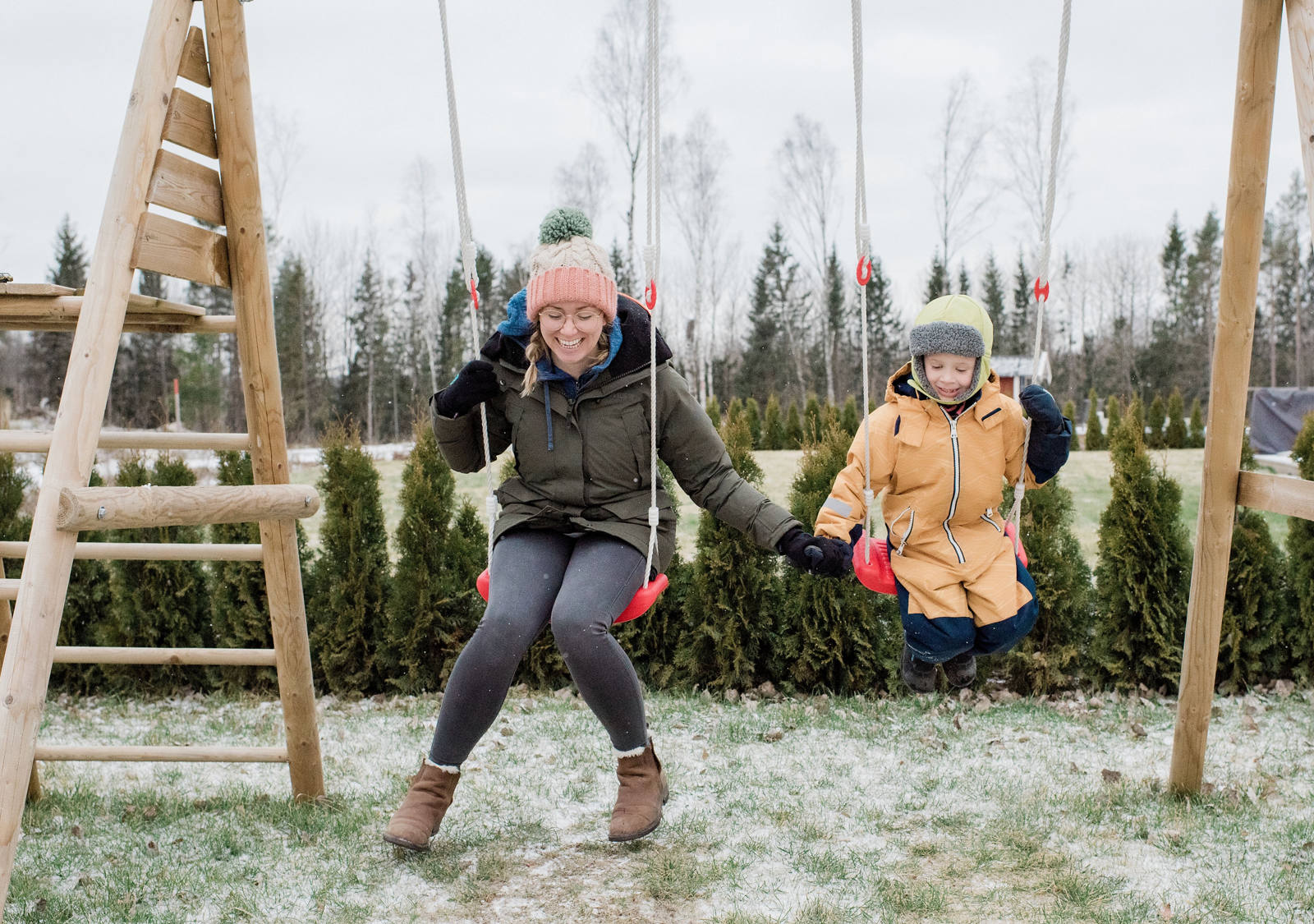 Woman with child warmly wrapped in winter clothes on a swing.