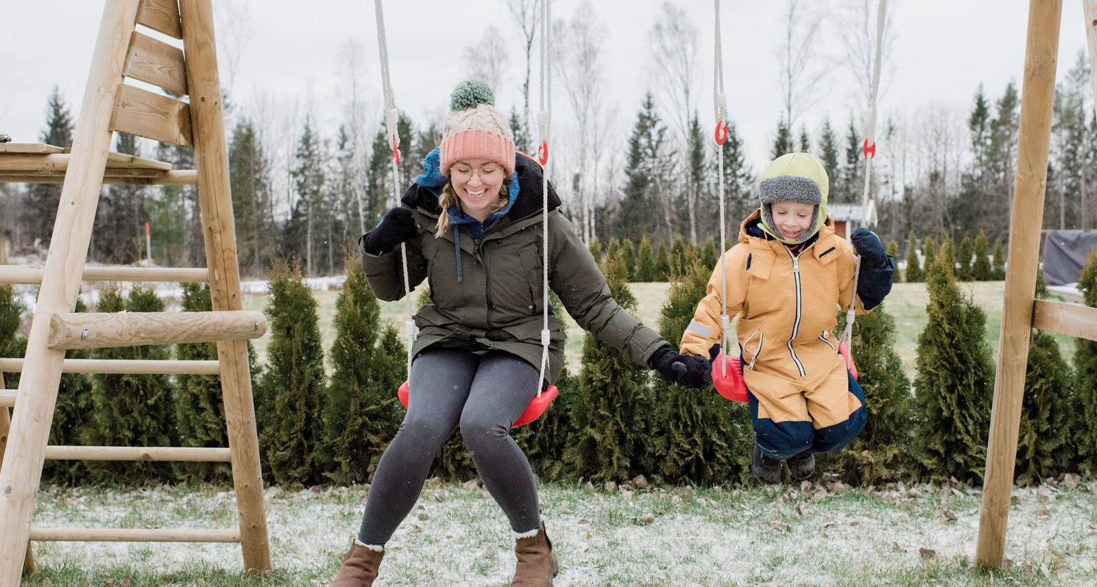 Frau mit Kind warm eingepackt in Winterkleidung auf einer Schaukel.