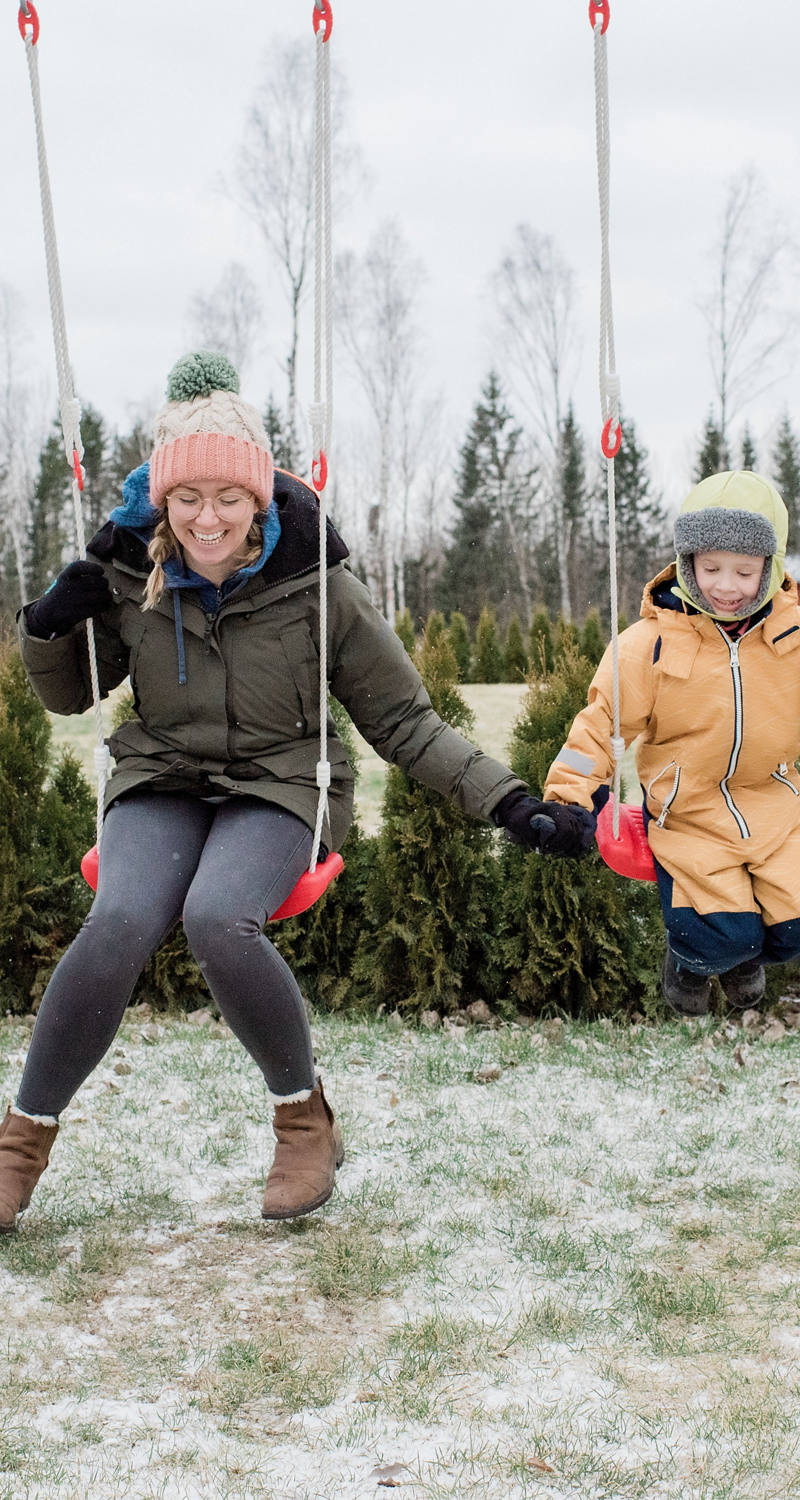Woman with child warmly wrapped in winter clothes on a swing.