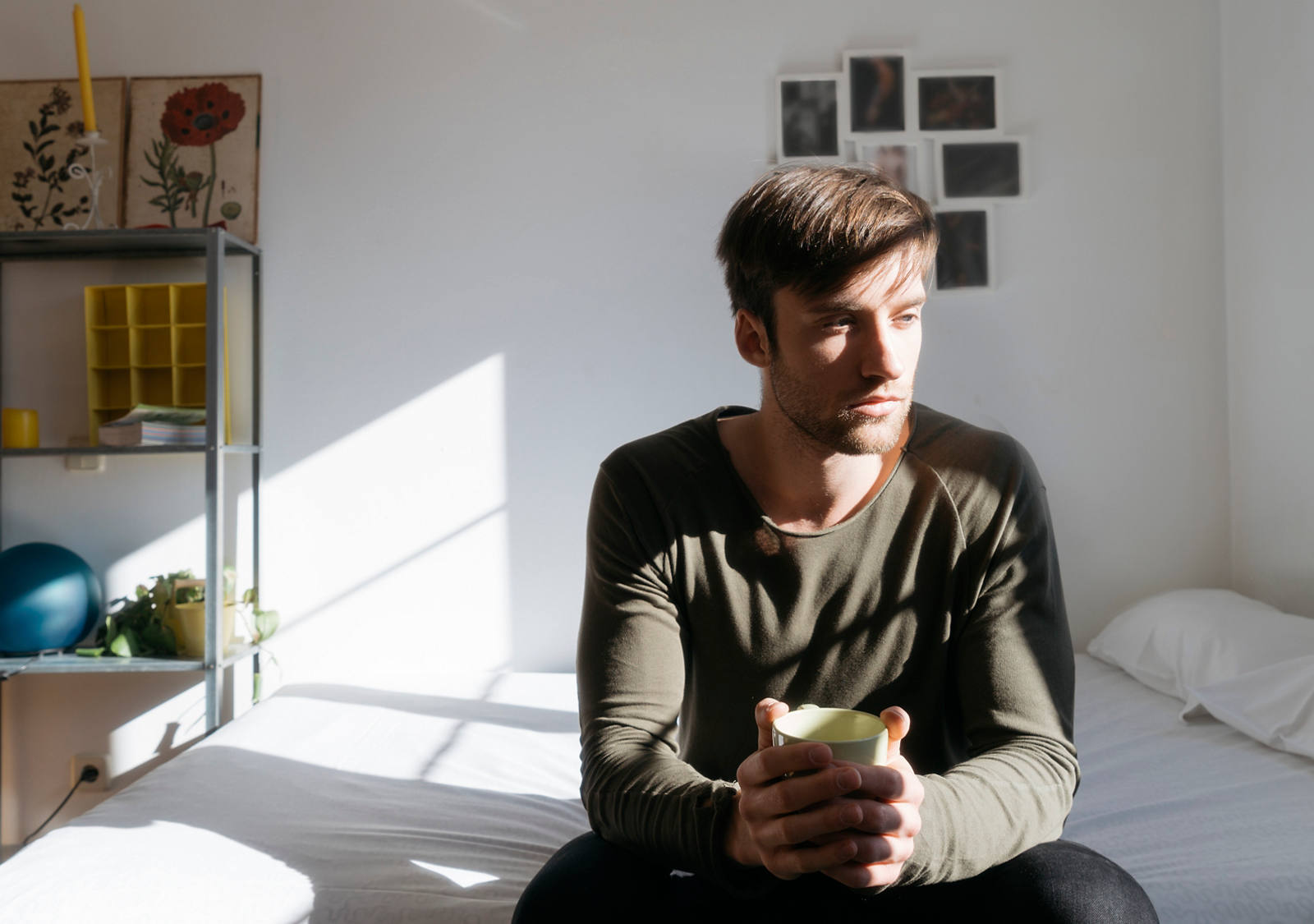 A man sits on the bed and looks into the distance thoughtfully.