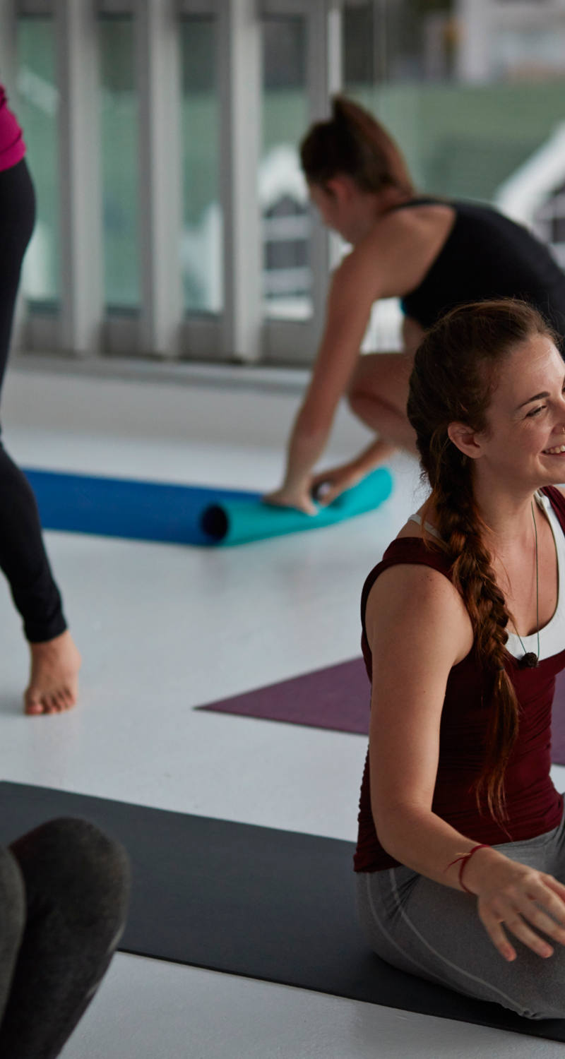 Gruppo di yoga al centro del quale una partecipante sorride cordialmente.