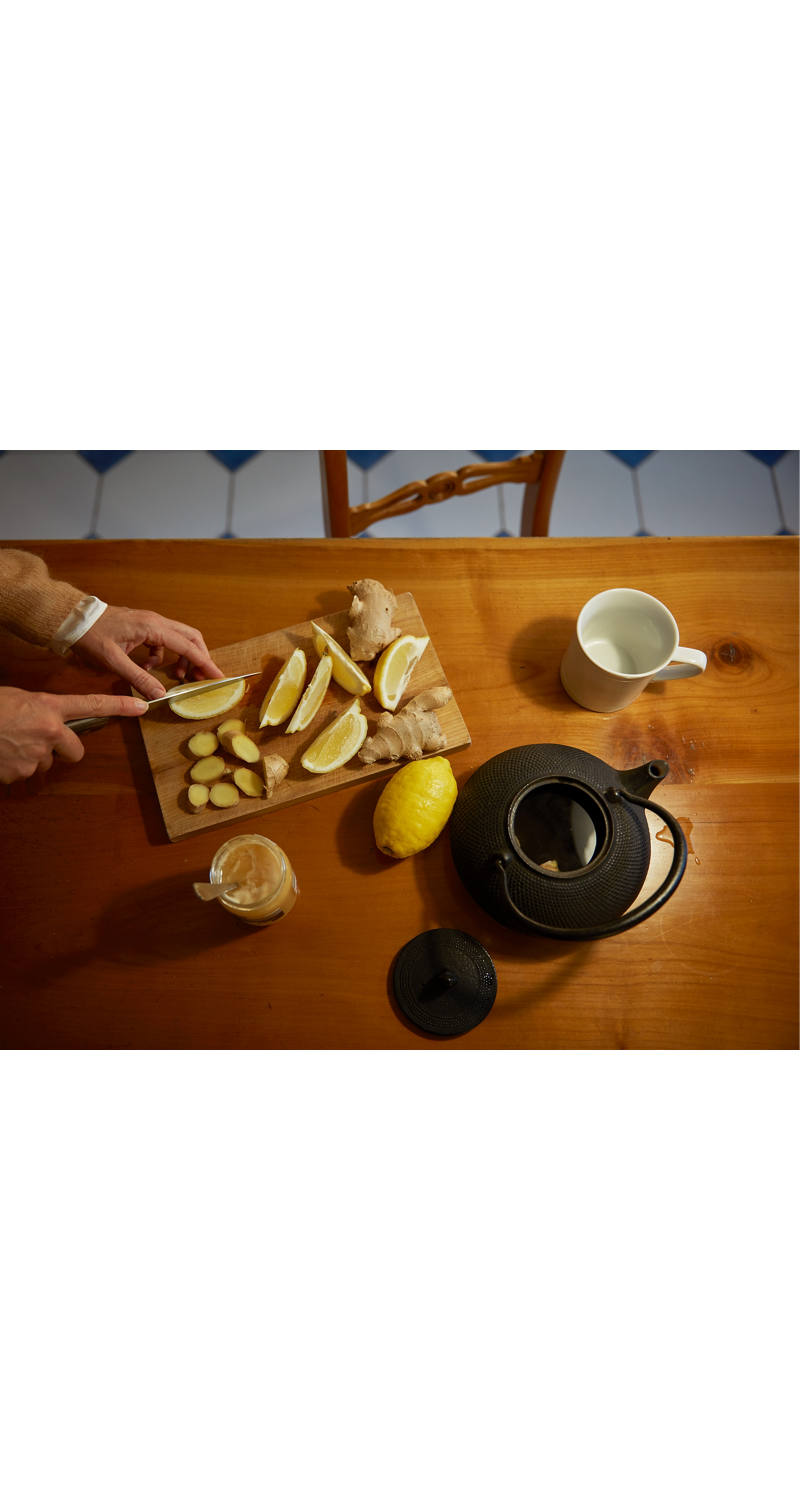Jemand schneidet Zitronen und Ingwer in Stücke und bereitet mit Honig und heissem Wasser einen Tee zu.